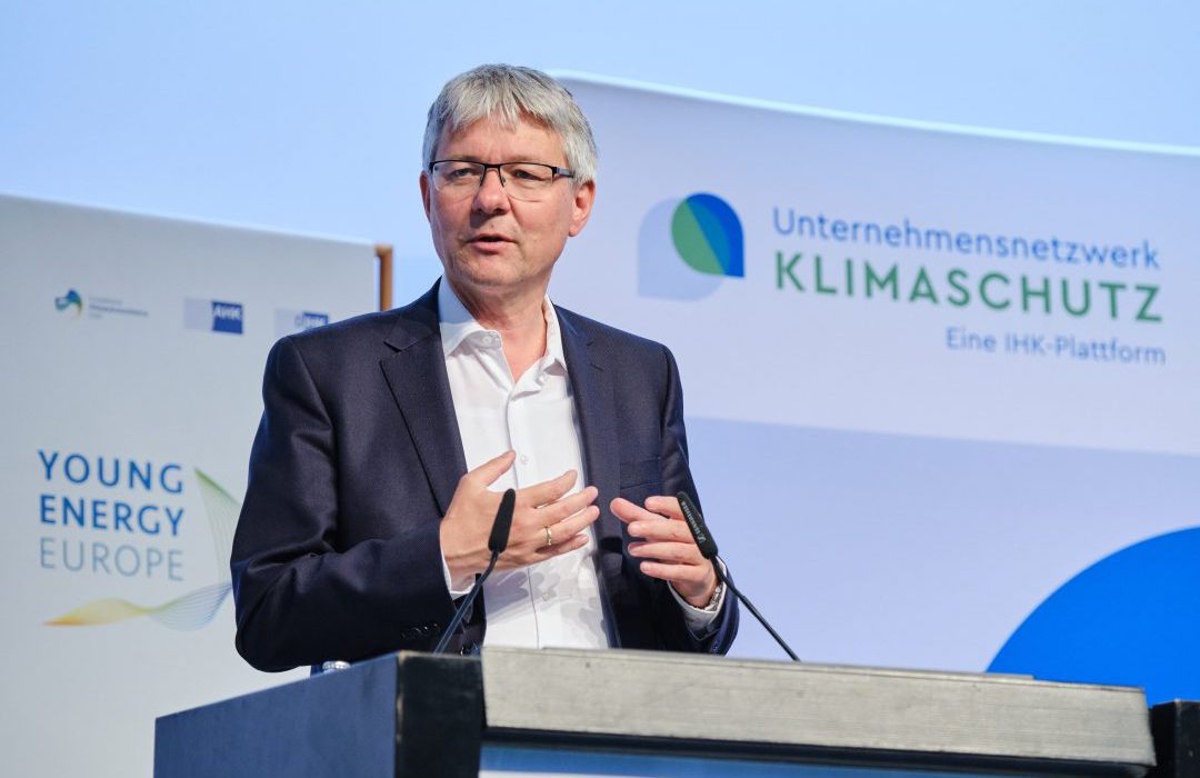 Achim Dercksl talking to a microphone, in the background "Young Energy Europe" and "Unternehmensnetzwerk Klimaschutz" Logos