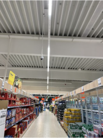A supermarket aisle, shelves with goods on the left and right, LED light strip above, with every third light switched off