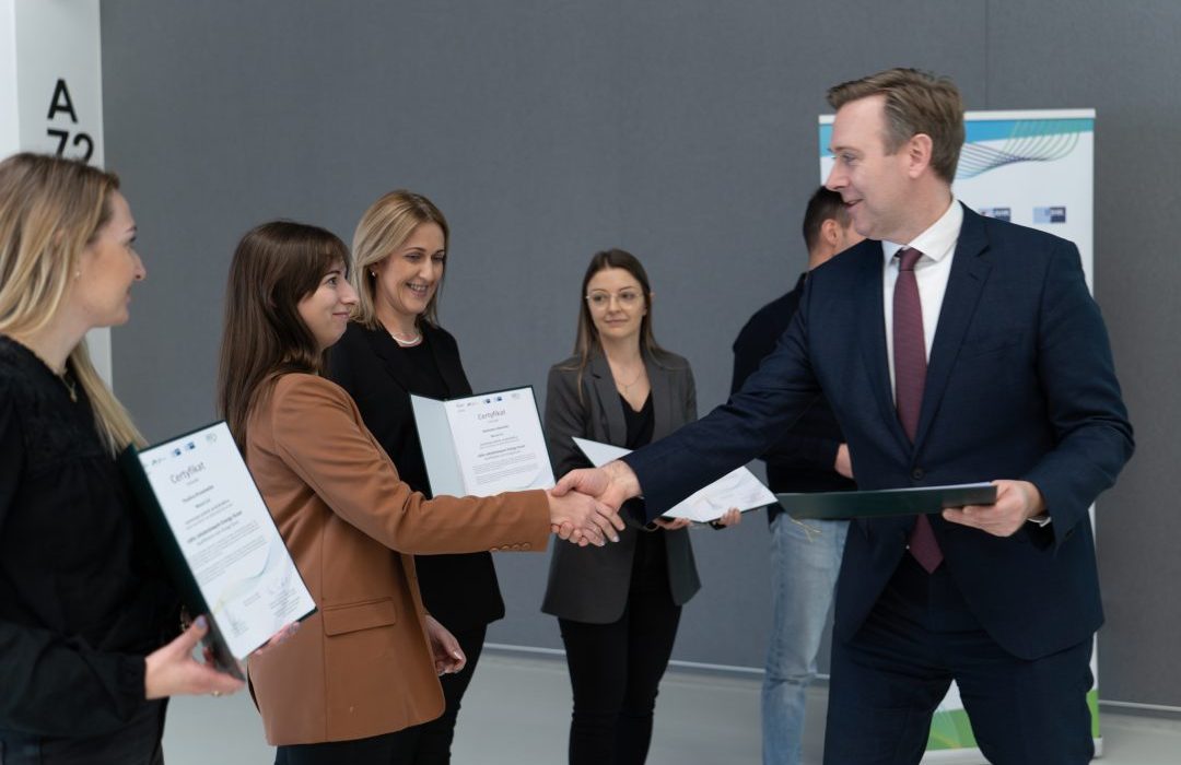 A man shakes hands with a woman, next to him three women holding certificates