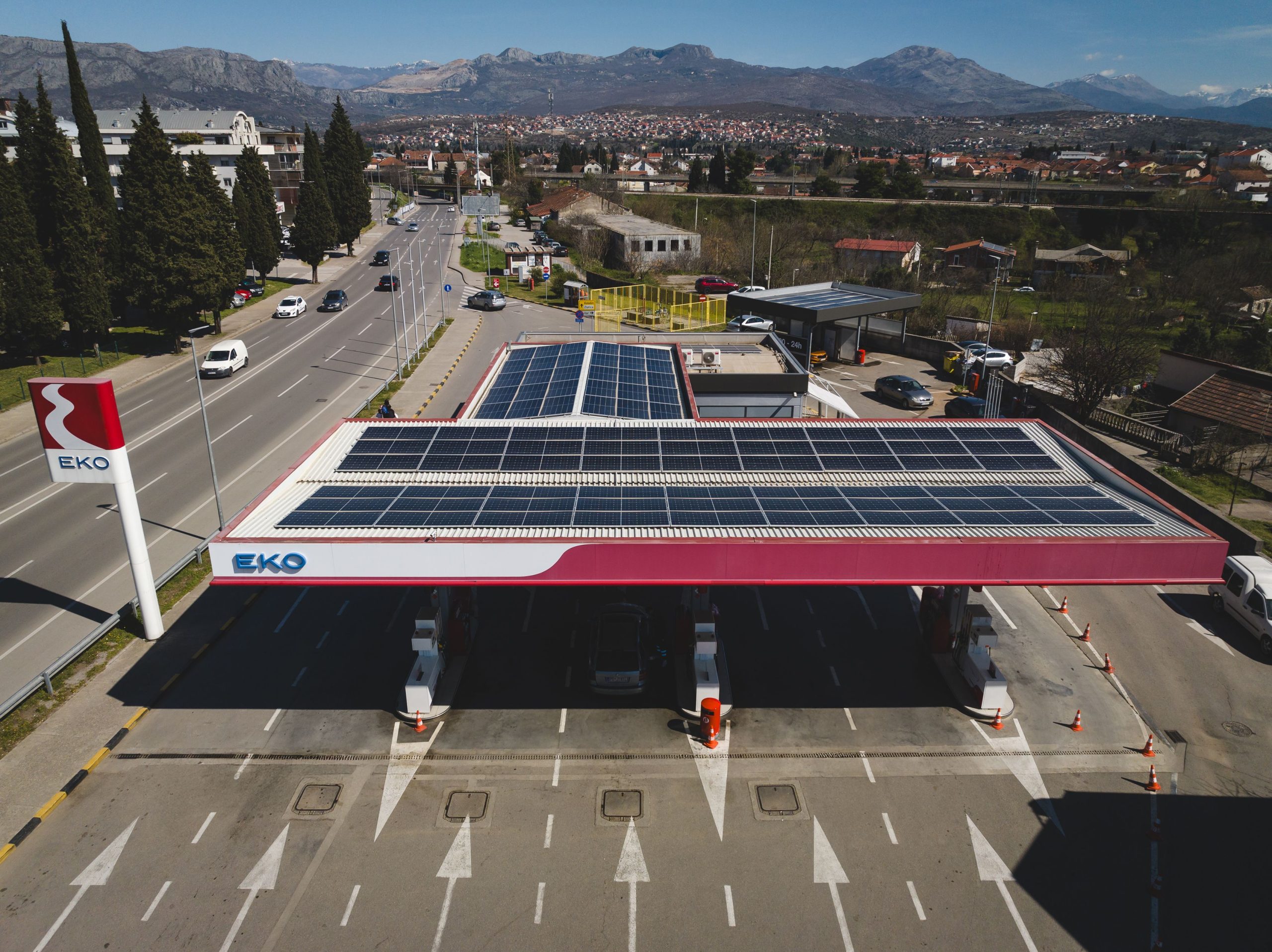 Tankstelle der Firma EKO im neben einer mehrspurigen Straße. Auf dem Dach der Station sind Sonnenpanelen angebracht. Im Hintergrund der Tankstelle sind Berge zu sehen.