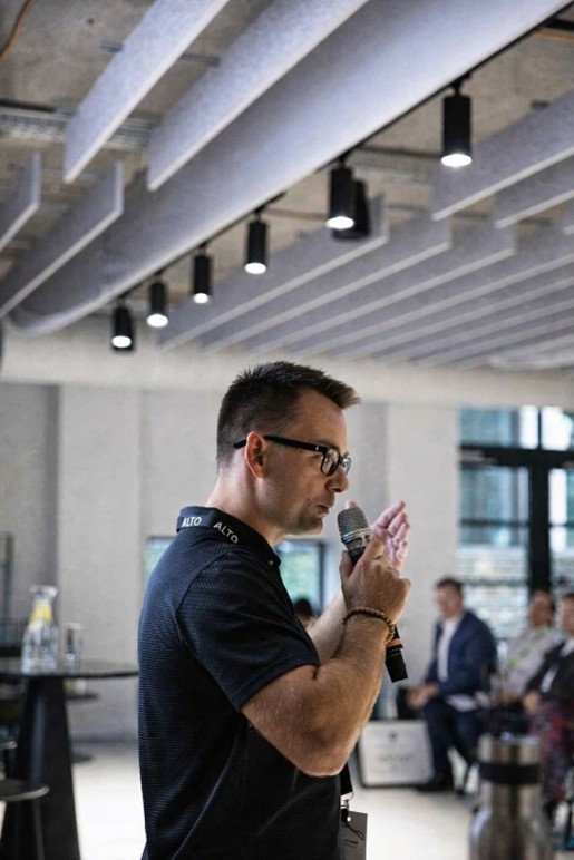 Im Bild sieht man den CEO der Firma, Michal Urban in ein Mikrofon vor einem Publikum sprechen.